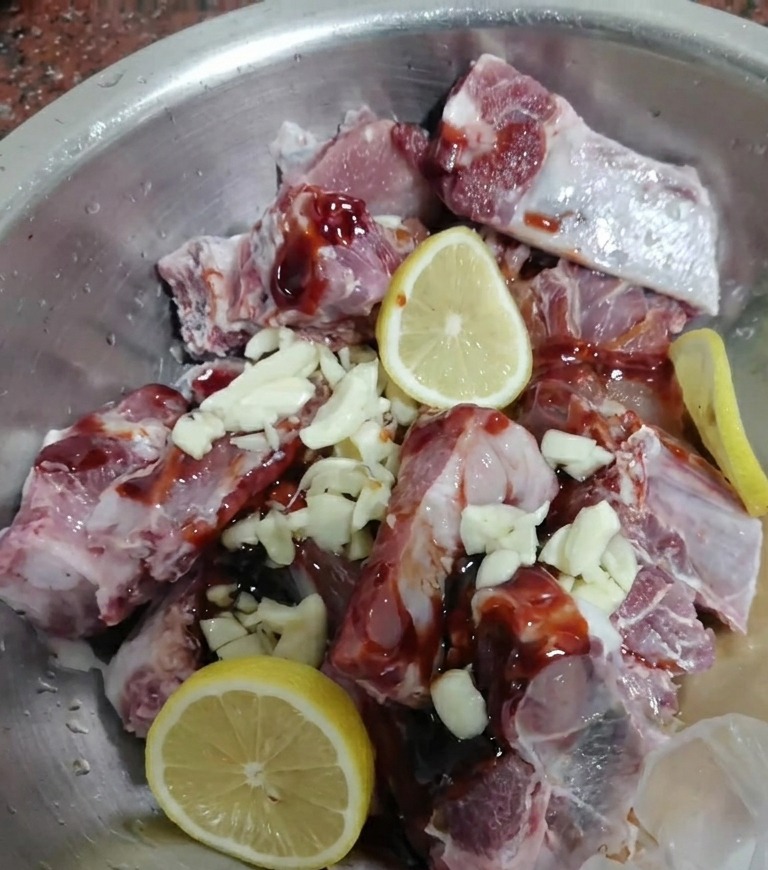 Travers de porc crus mélangés avec une marinade foncée, de lail et des tranches de citron frais.