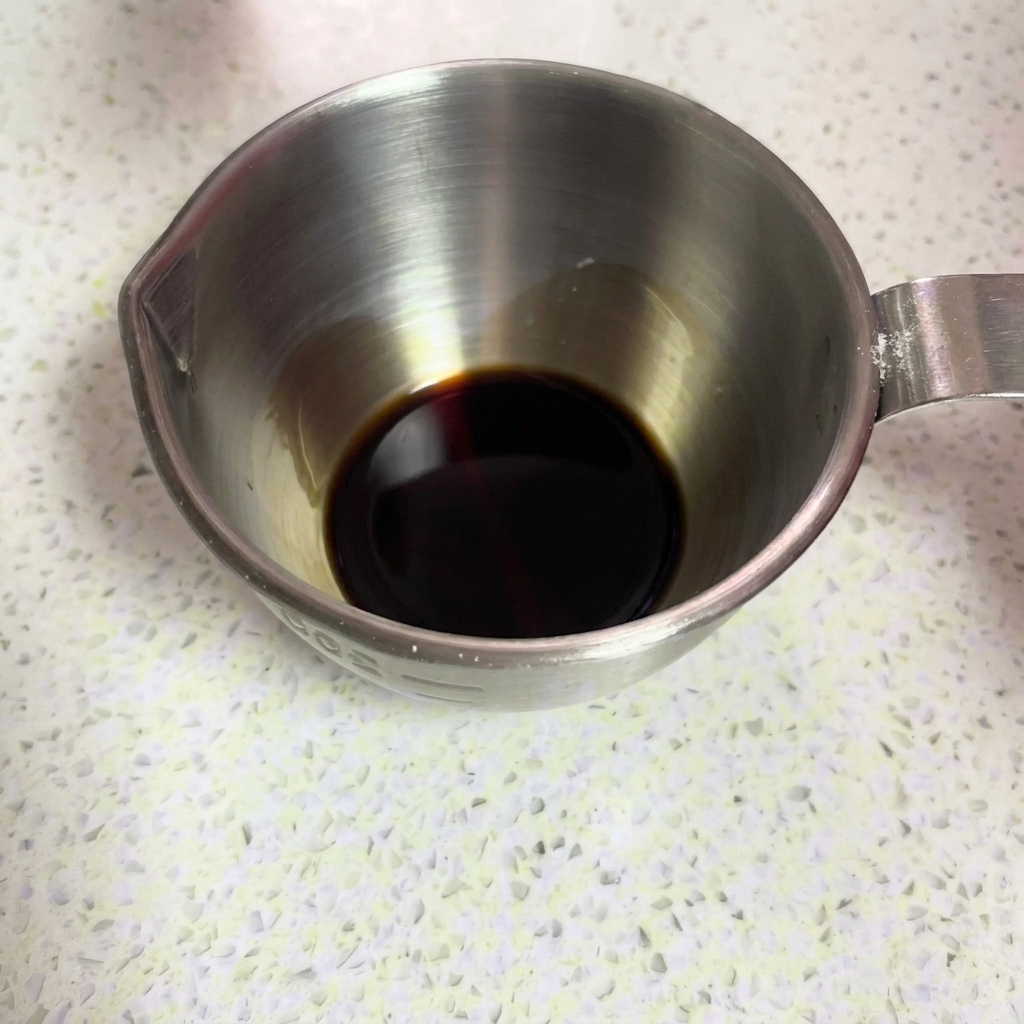 De la sauce soja noire versée dans un récipient doseur en métal.