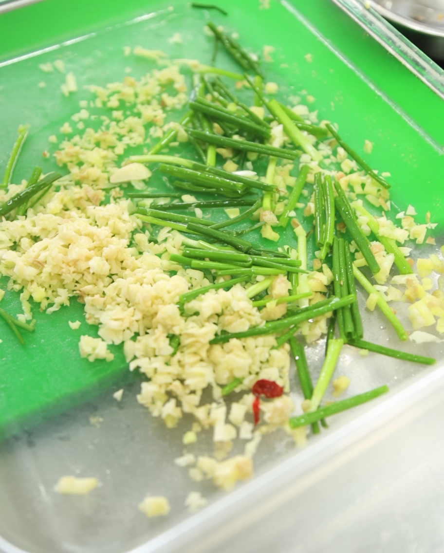 Un récipient contenant de lail frais émincé, de la ciboulette fraîchement hachée et une généreuse dose de pâte de piment rouge vif.