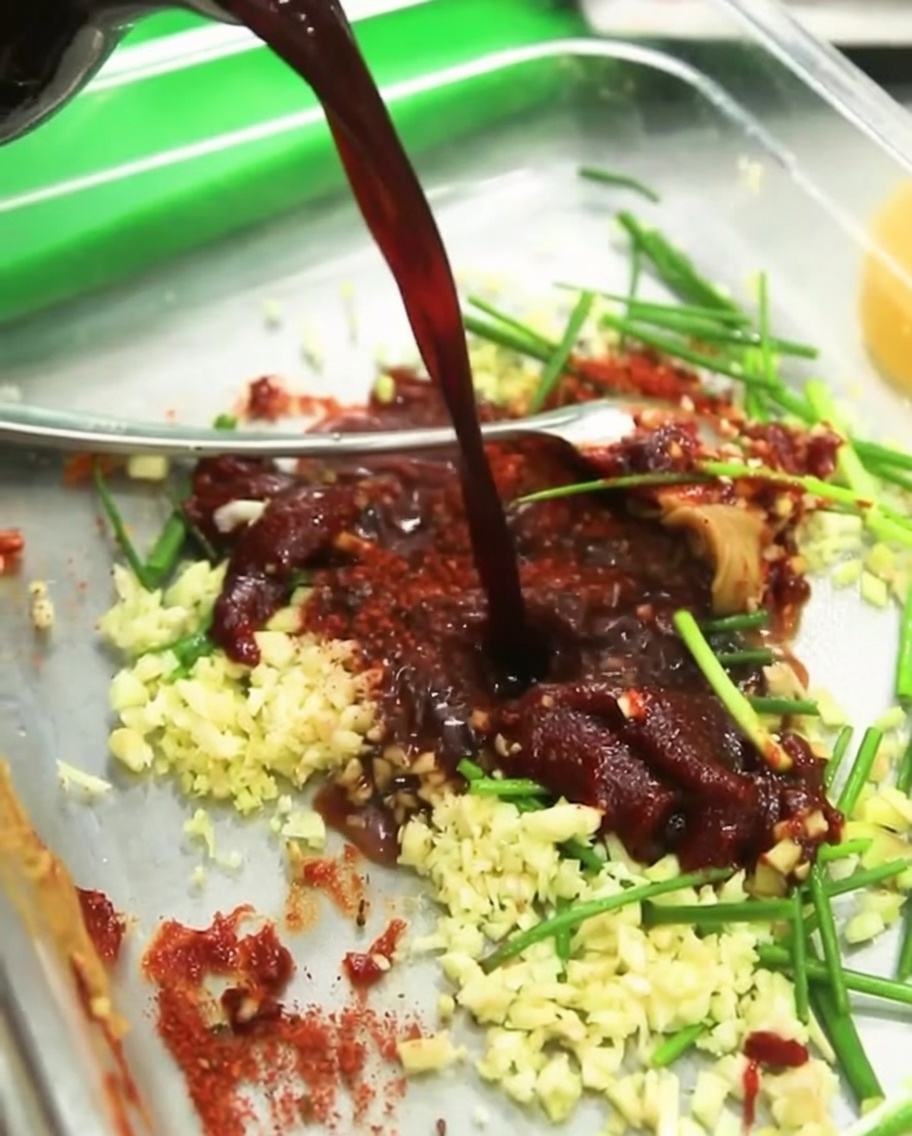 Du vin de cuisine clair versé dans le bol de marinade, se mélangeant à la sauce soja et aux aromates.