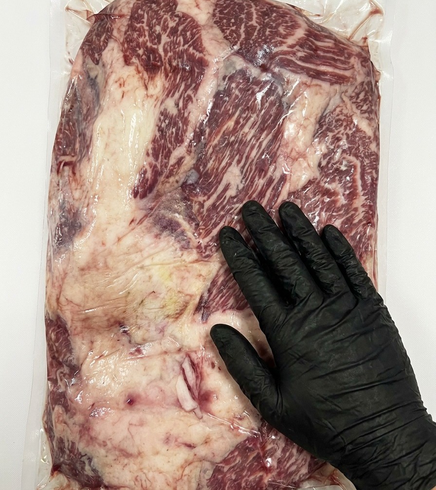 Gros plan dun couteau retirant lexcès de gras de la surface dune poitrine crue de bœuf Stone Axe Wagyu.