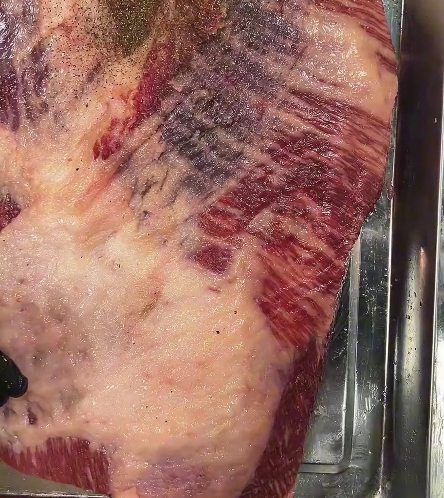 Poivre noir concassé saupoudré généreusement sur la surface de la poitrine crue salée.
