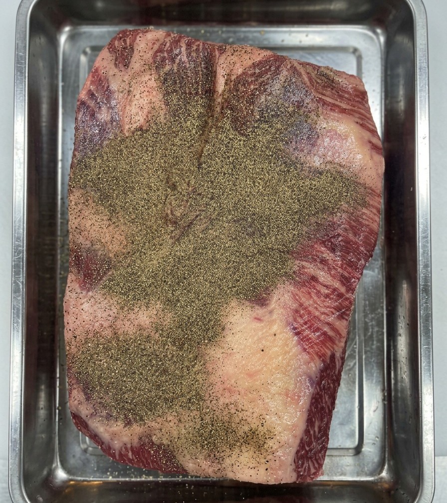 Mains gantées pressant le poivre noir sur la poitrine de Wagyu pour créer une couche dassaisonnement homogène.