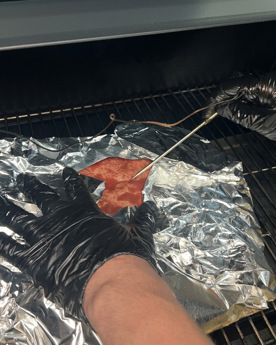 La poitrine emballée replacée sur les grilles du fumoir avec la sonde du thermomètre réinsérée.