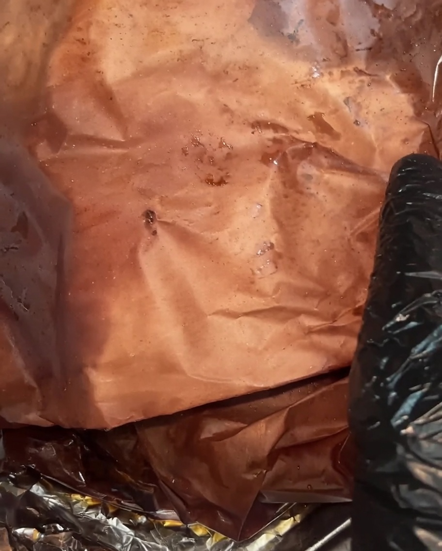 La poitrine entièrement cuite déballée, révélant une croûte sombre et luisante, avec un abondant jus accumulé dans le papier de boucher.