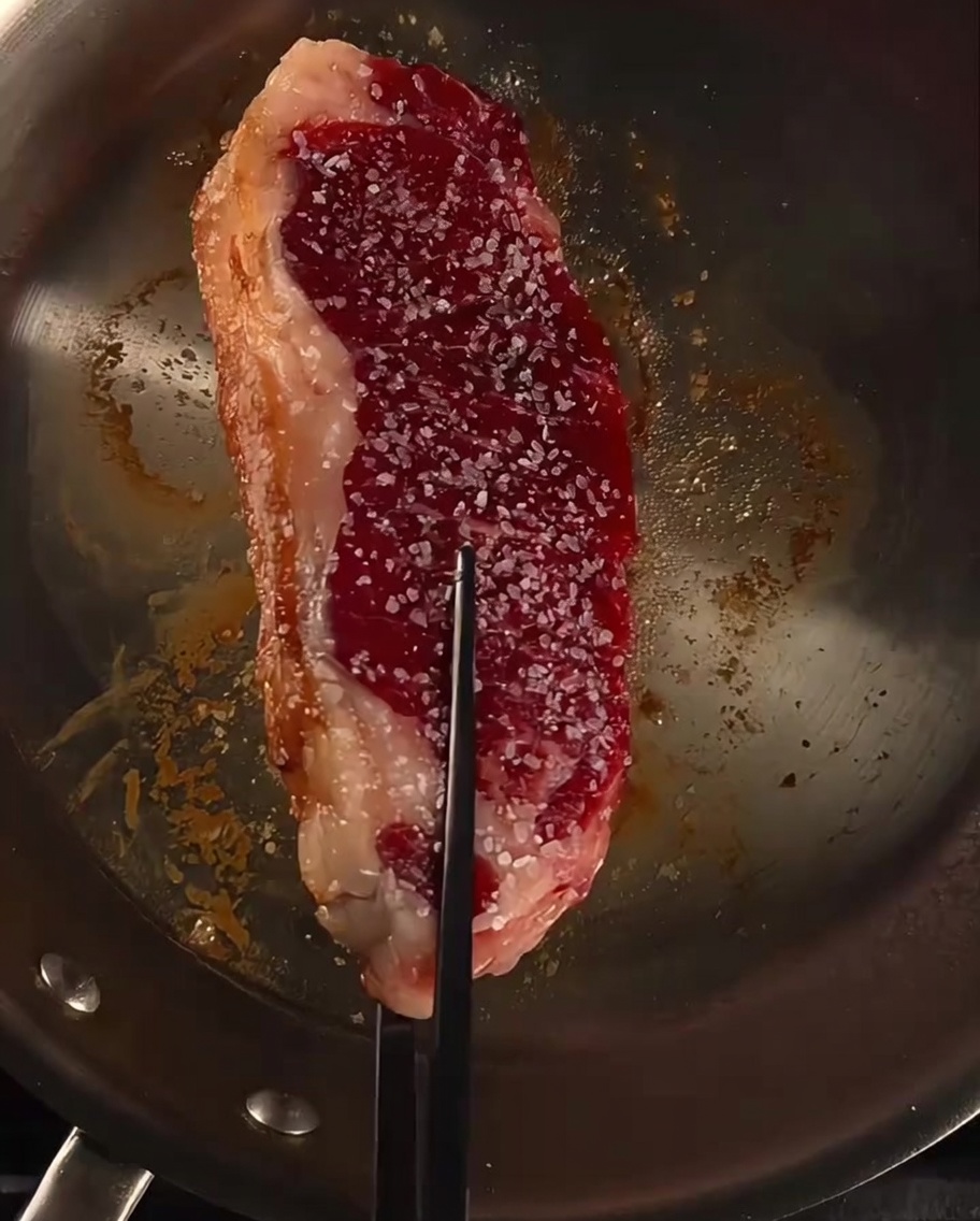 Steak dans une poêle arrosé de beurre, dail et de brins de romarin frais.