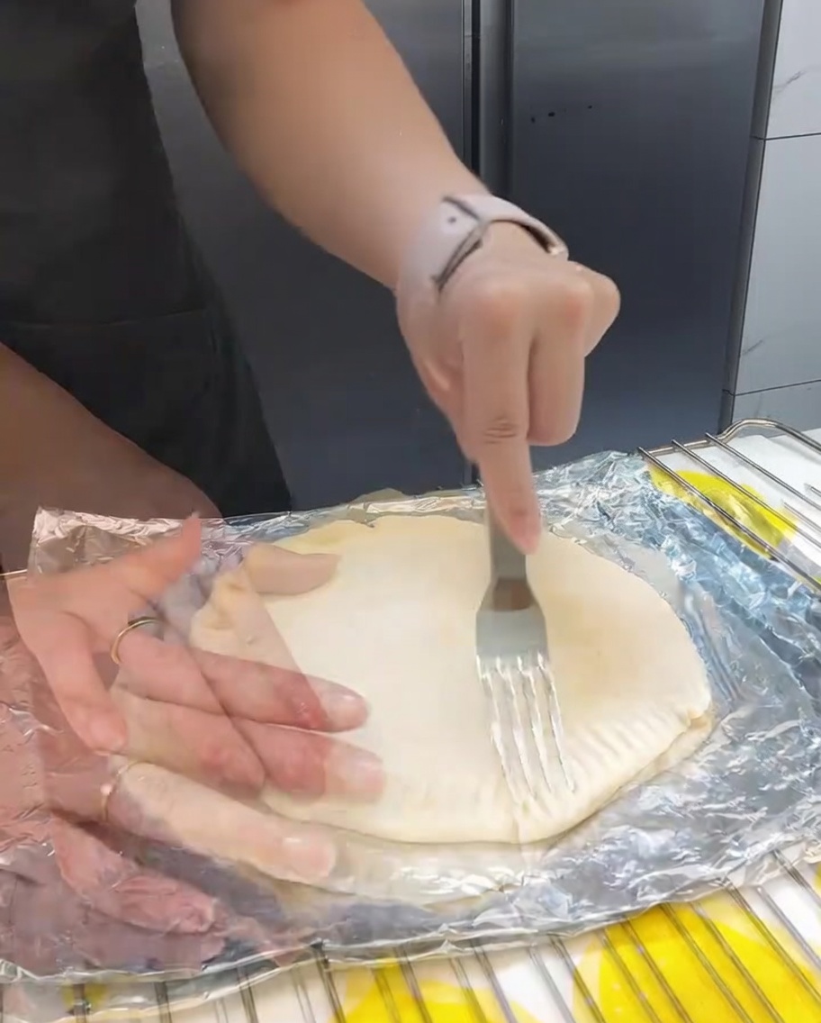 Fourchette pinçant les bords des galettes à la ciboule empilées pour créer une bordure décorative et fonctionnelle.