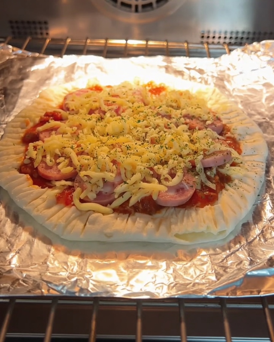 Une pizza sur galette à la ciboule fraîchement cuite avec du fromage fondu et des tranches de saucisse, dans le four sur une grille.