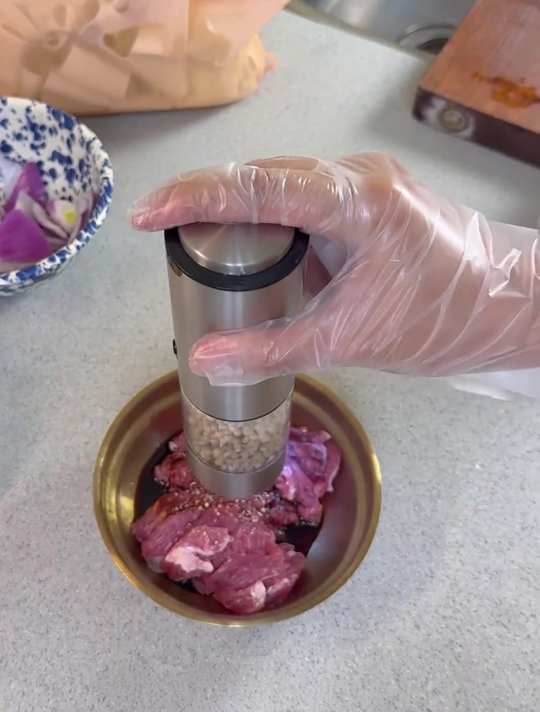 Moulin à poivre électrique saupoudrant du poivre frais sur des tranches de porc cru mélangées à de la sauce soja dans un petit bol en métal.