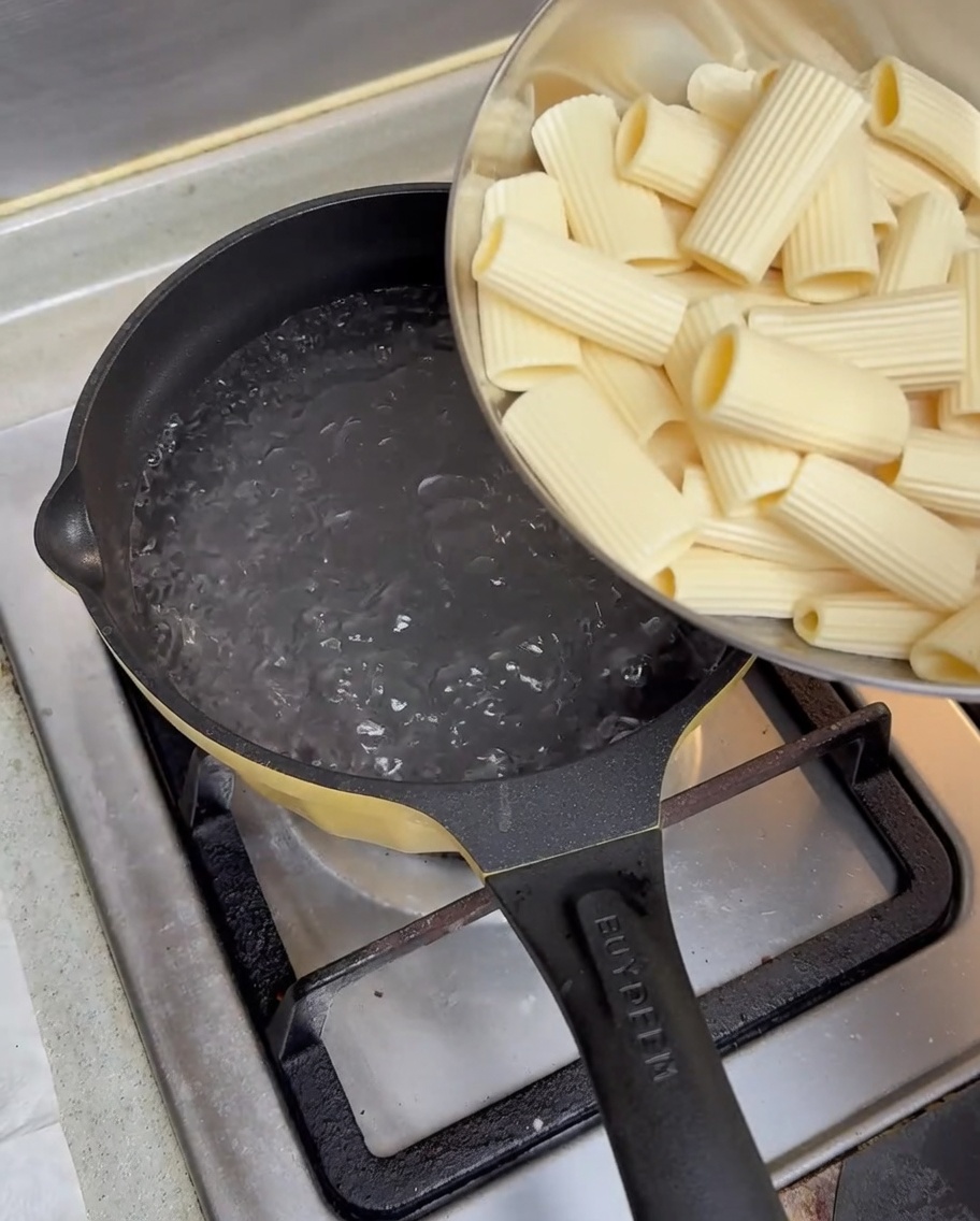 Rigatoni pré-trempés versés dun bol en métal dans une casserole deau bouillante sur une cuisinière à gaz.