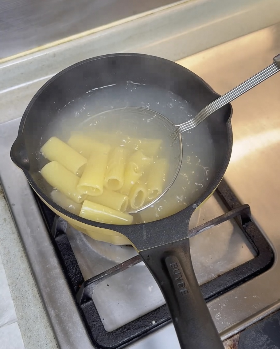 Une écumoire en fil métallique retirant les rigatoni cuits dune casserole noire.