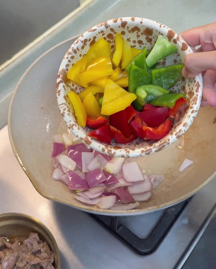 Morceaux de poivrons rouges, jaunes et verts ajoutés à la poêle contenant les oignons sautés.