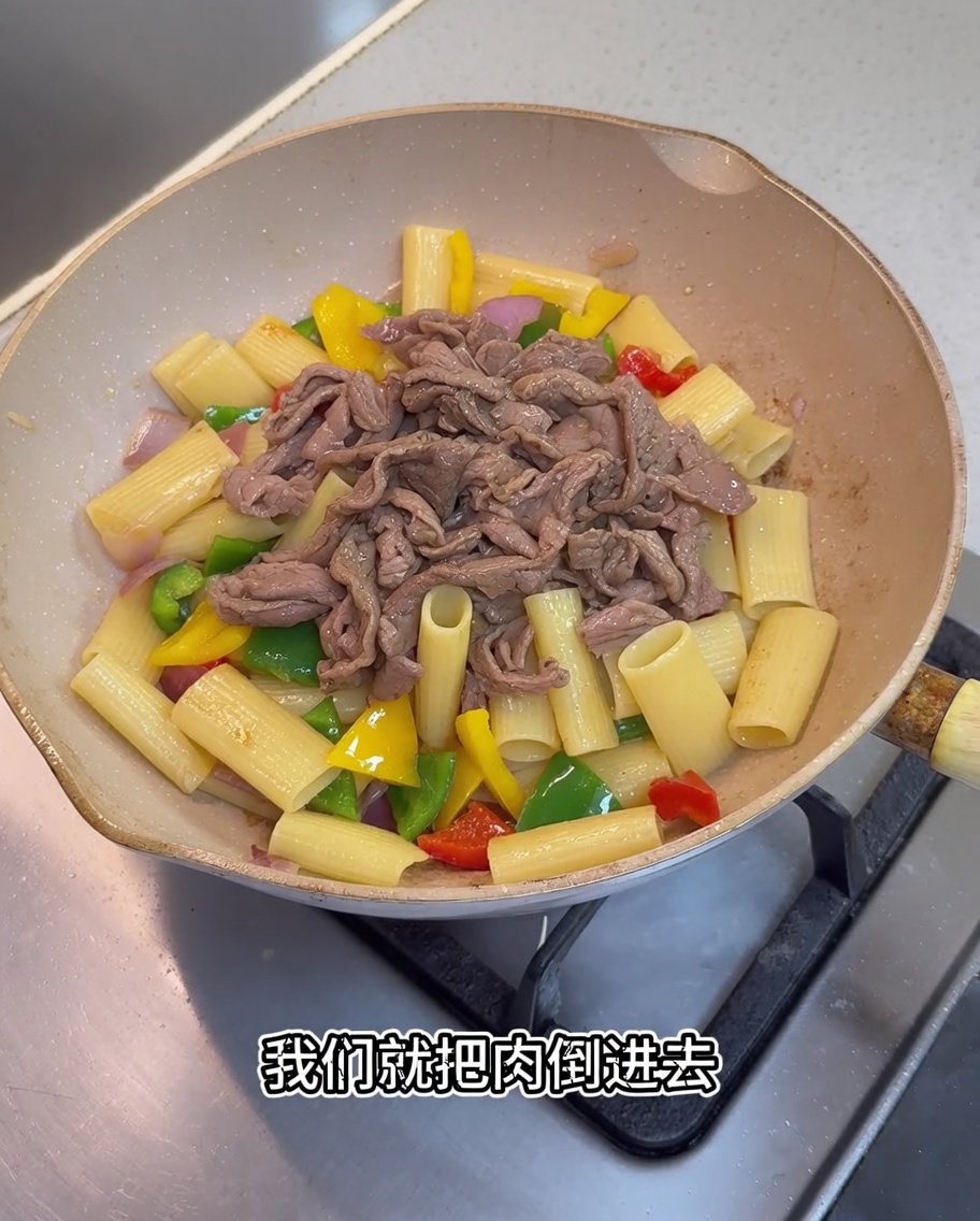 Morceaux de porc cuits et sauce sombre ajoutés à la poêle contenant les rigatoni et les légumes.