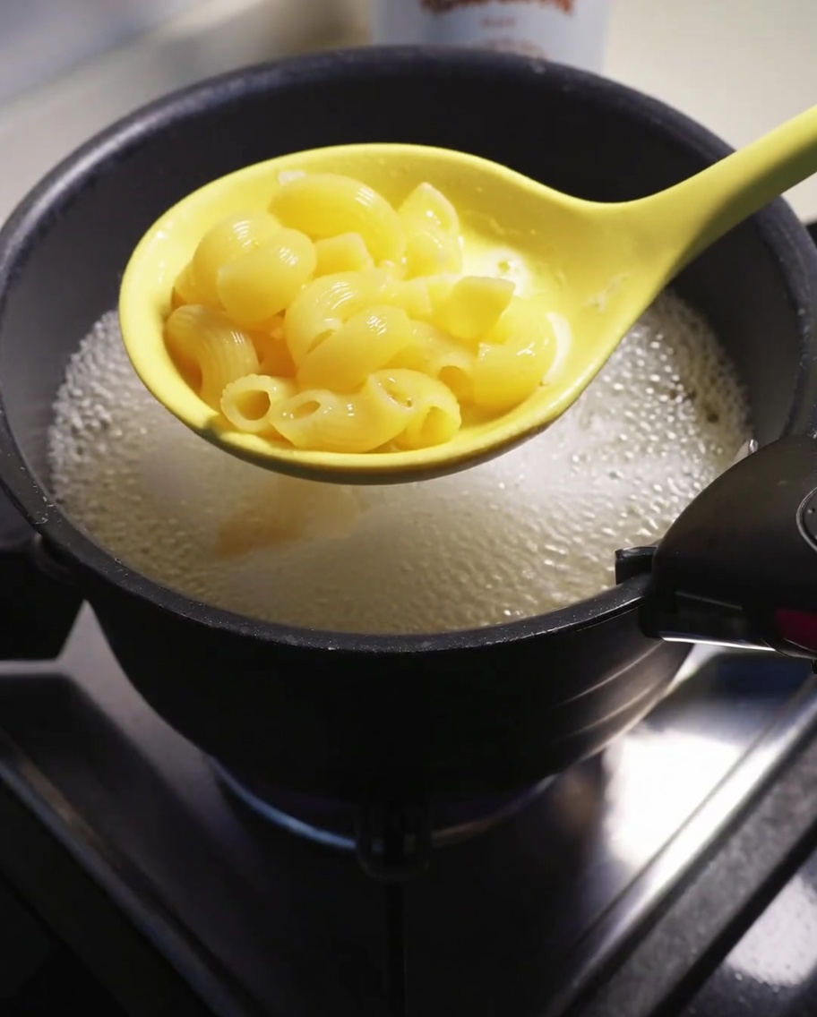 Macaronis cuits retirés de leau bouillante avec une écumoire jaune.
