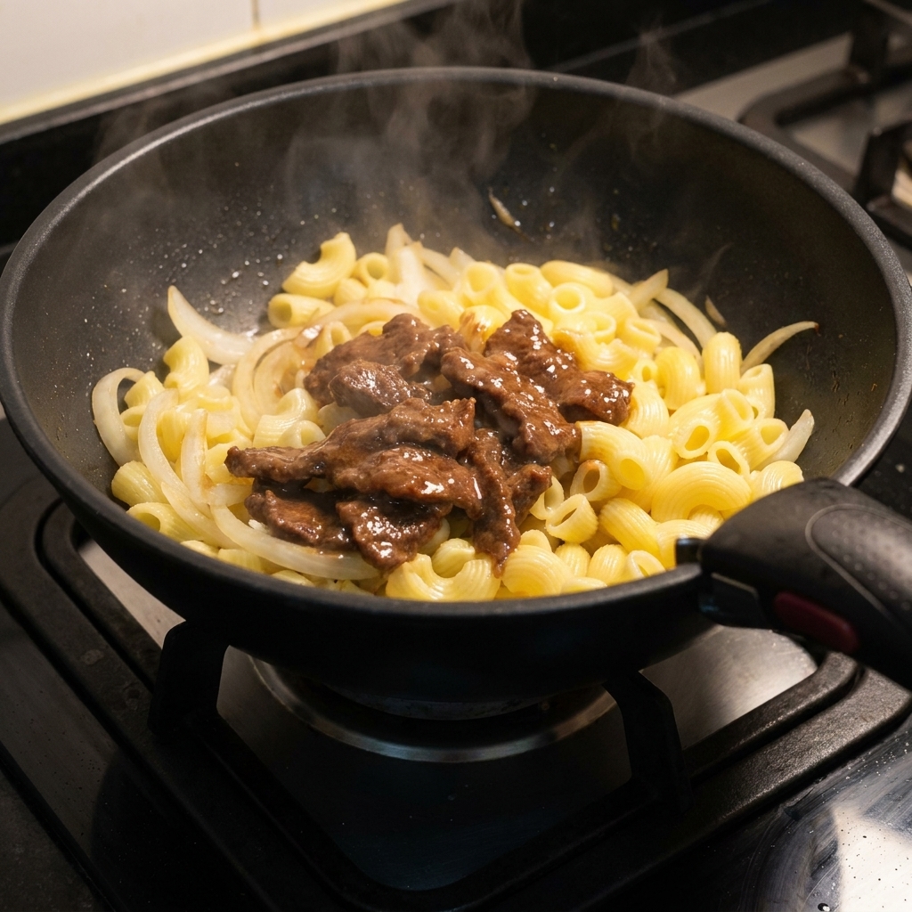 Tranches de bœuf saisies remises dans la poêle sur les macaronis et les oignons.