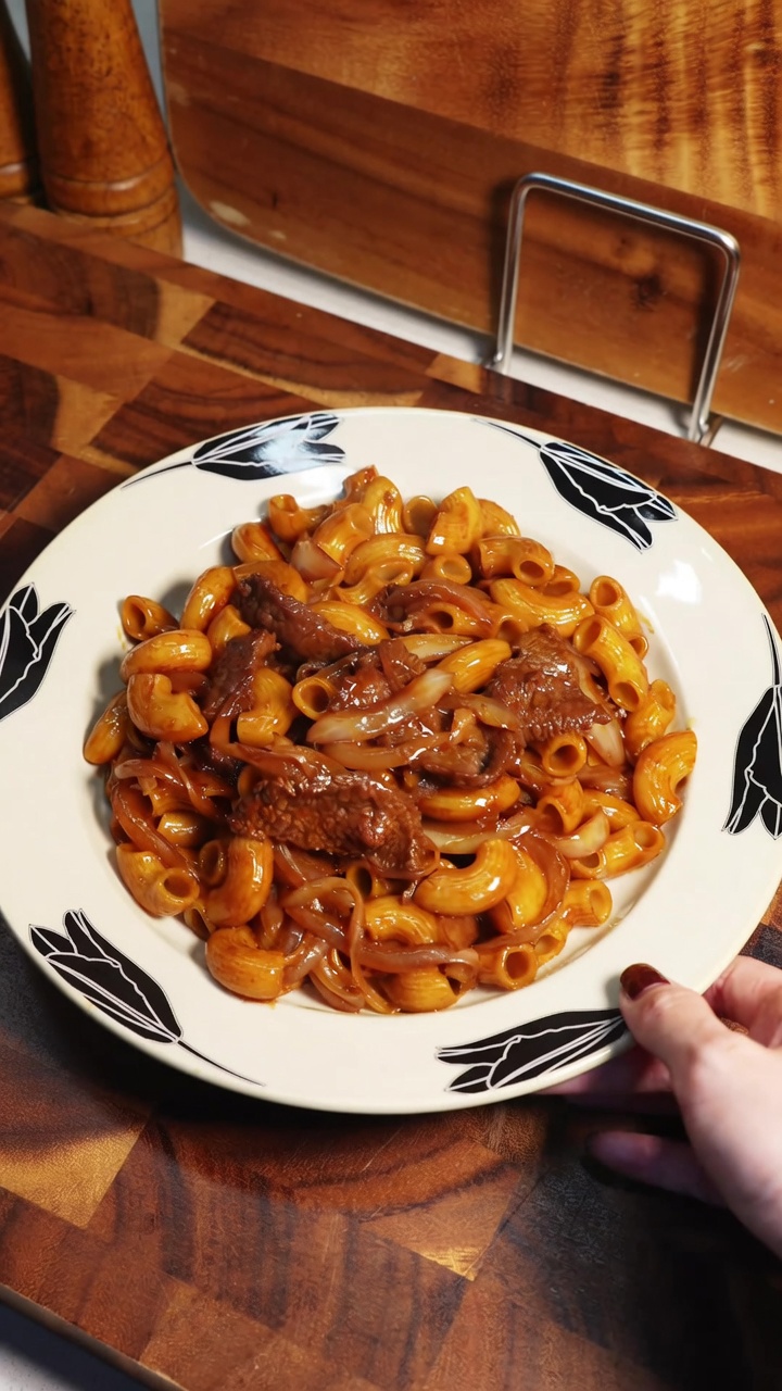 Une portion de macaronis sautés au bœuf, agrémentée doignons translucides.