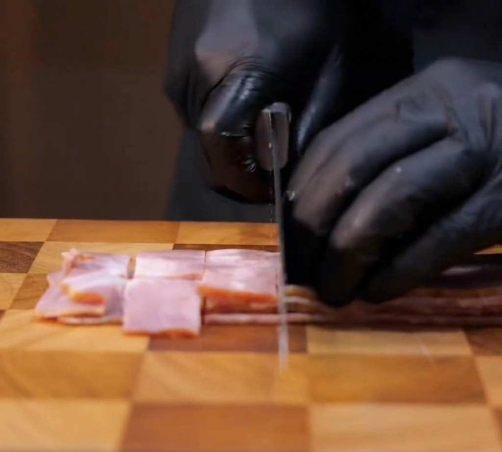 Tranches de bacon coupées en carrés sur une planche à découper.