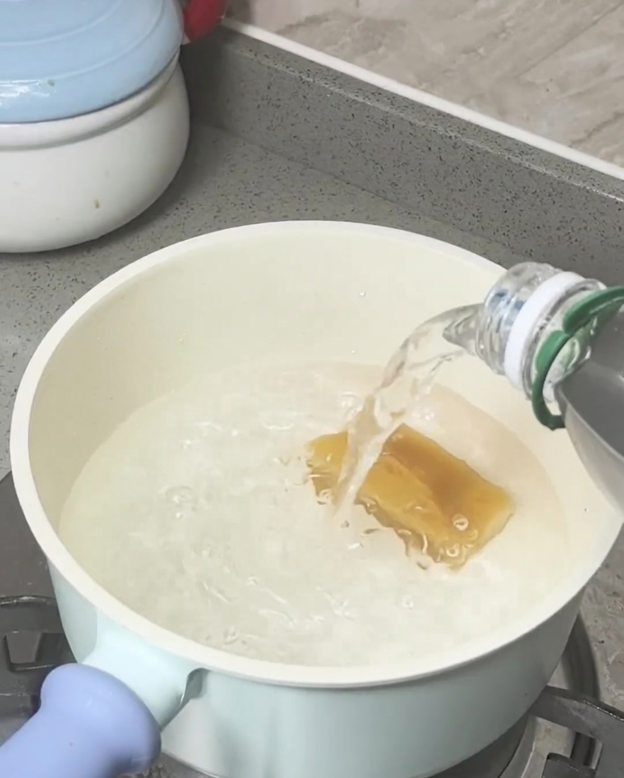 Bloc de sucre roux fondant dans de leau bouillante dans une casserole de couleur claire.