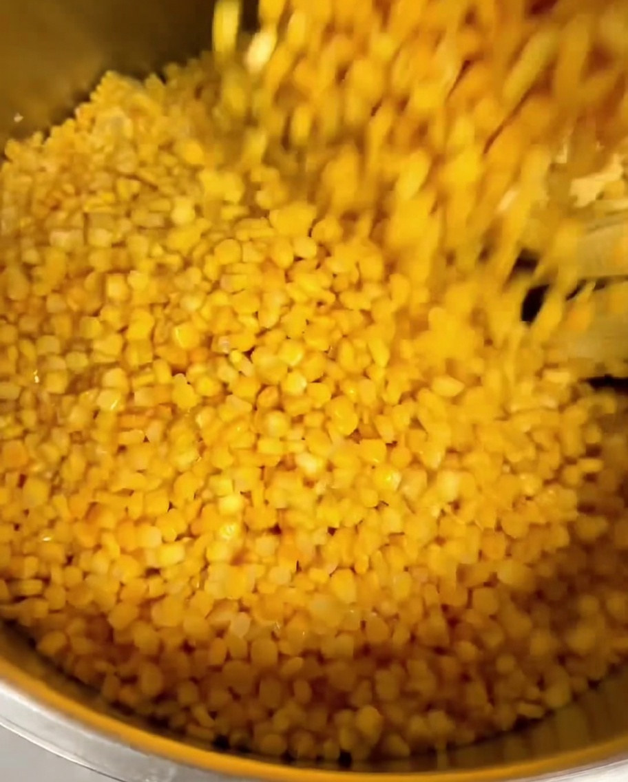 Maïs en conserve versé sur des grains de maïs frais dans une grande casserole en métal.