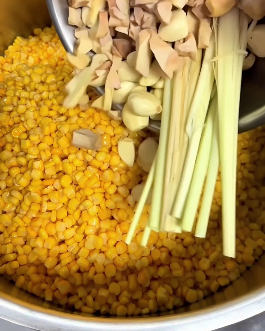 Galanga haché, gousses dail entières et tiges de citronnelle ajoutées dans une casserole.