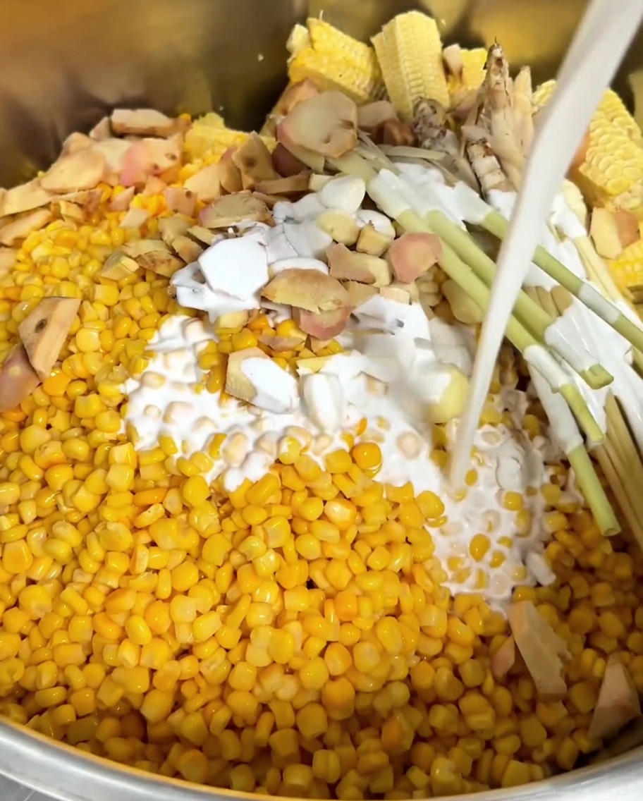 Lait de coco blanc versé sur le maïs, les aromates et les rafles de maïs dans une casserole.