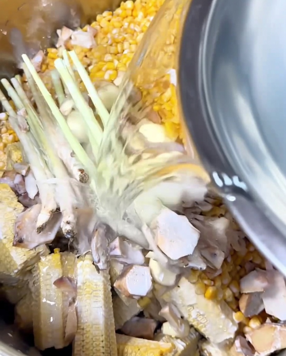 Eau claire versée dun bol en métal dans une casserole remplie de maïs, aromates et lait de coco.