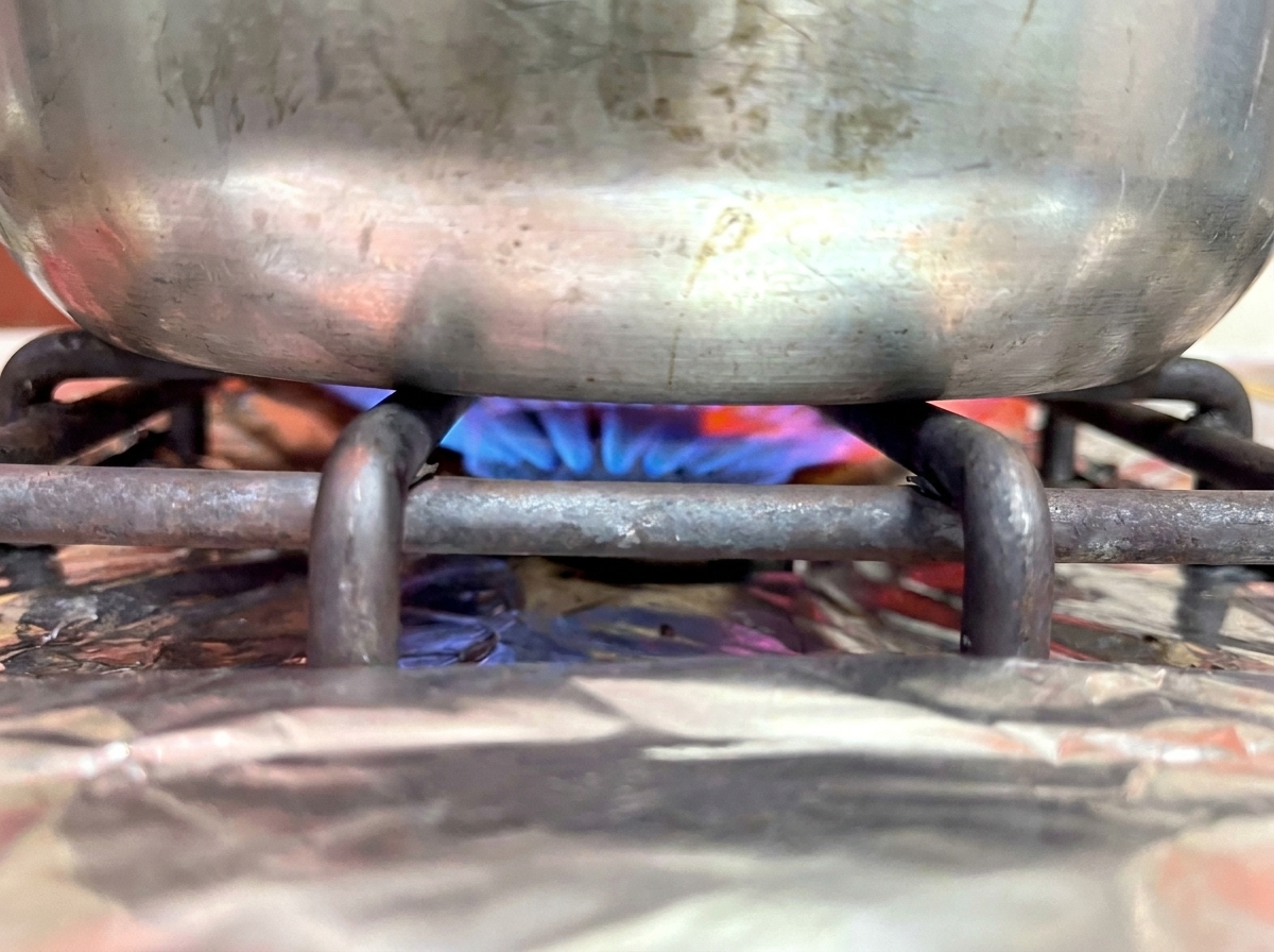 Le fond dune casserole en métal sur un brûleur de cuisinière à gaz avec une flamme bleue.