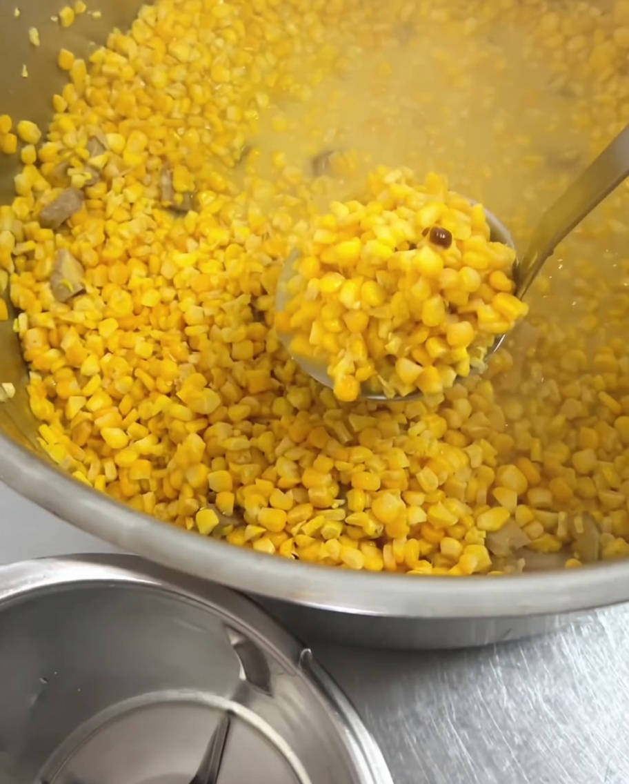 Une louche en métal prélevant les grains de maïs cuits dans la casserole.