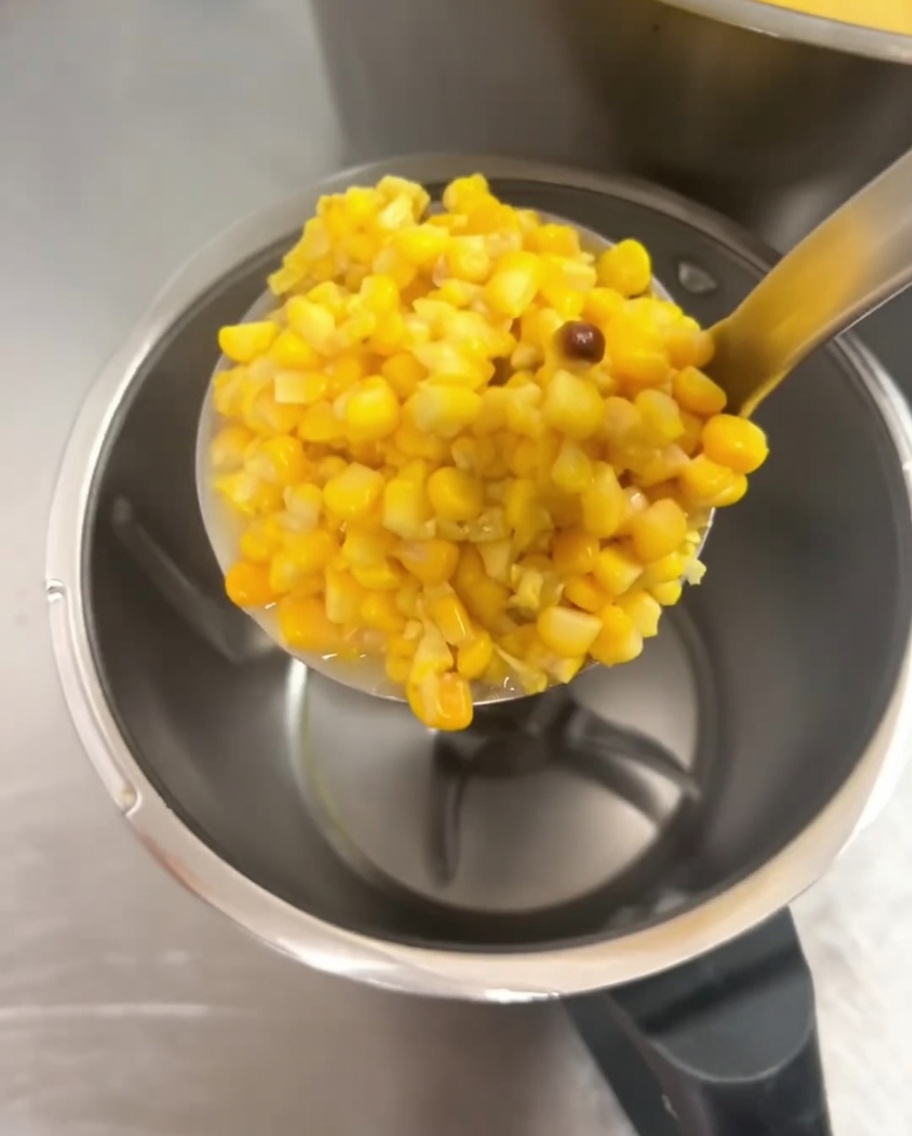 Grains de maïs cuits ajoutés dans un grand bol de mixeur.