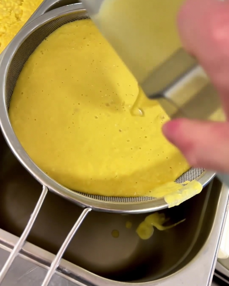 Soupe de maïs jaune passée à travers une passoire fine dans un récipient.