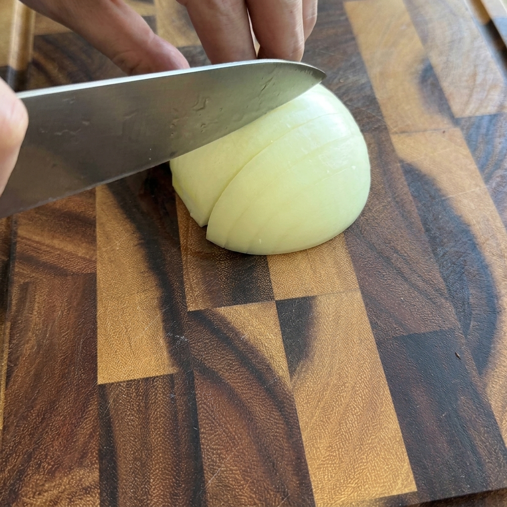 Une personne coupant un demi-oignon blanc en petits dés sur une planche à découper en bois.