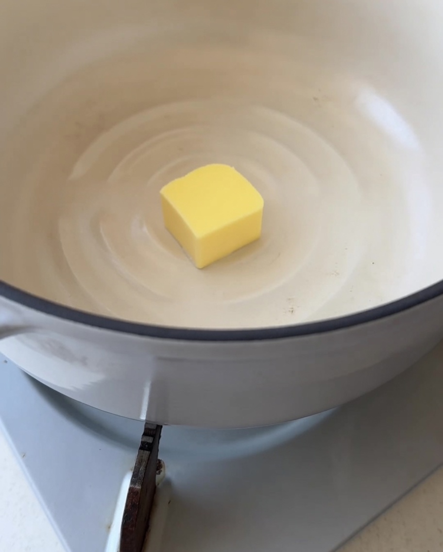 Gros plan dun carré de beurre jaune commençant à fondre dans une casserole blanche propre.