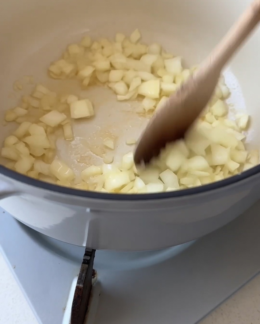 Une cuillère en bois mélangeant des dés doignon blanc dans une casserole blanche avec du beurre fondu.