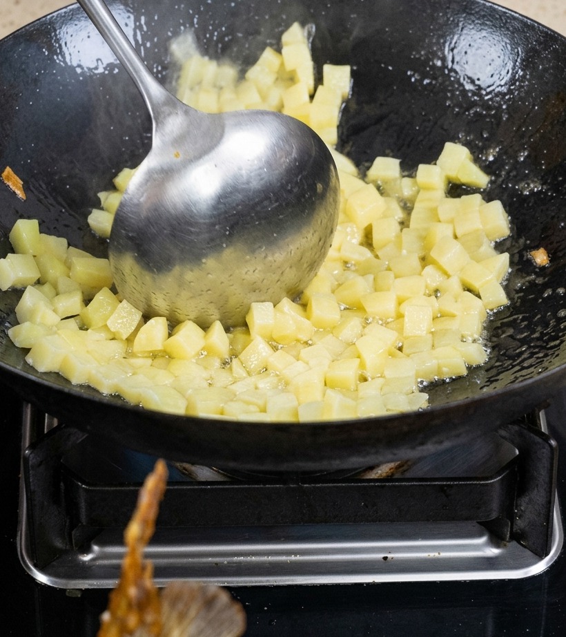 Dés de pommes de terre sautés dans un wok avec de lhuile jusquà coloration.