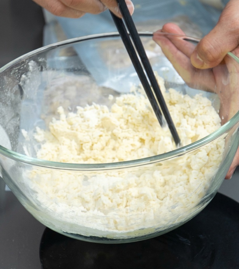 Bol contenant un mélange de farine et dœuf mélangé avec des baguettes pour former des miettes.