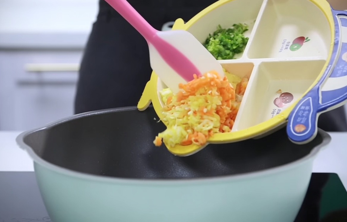 Des carottes, des pommes de terre et du céleri coupés versés dune assiette compartimentée pour bébé dans une casserole.
