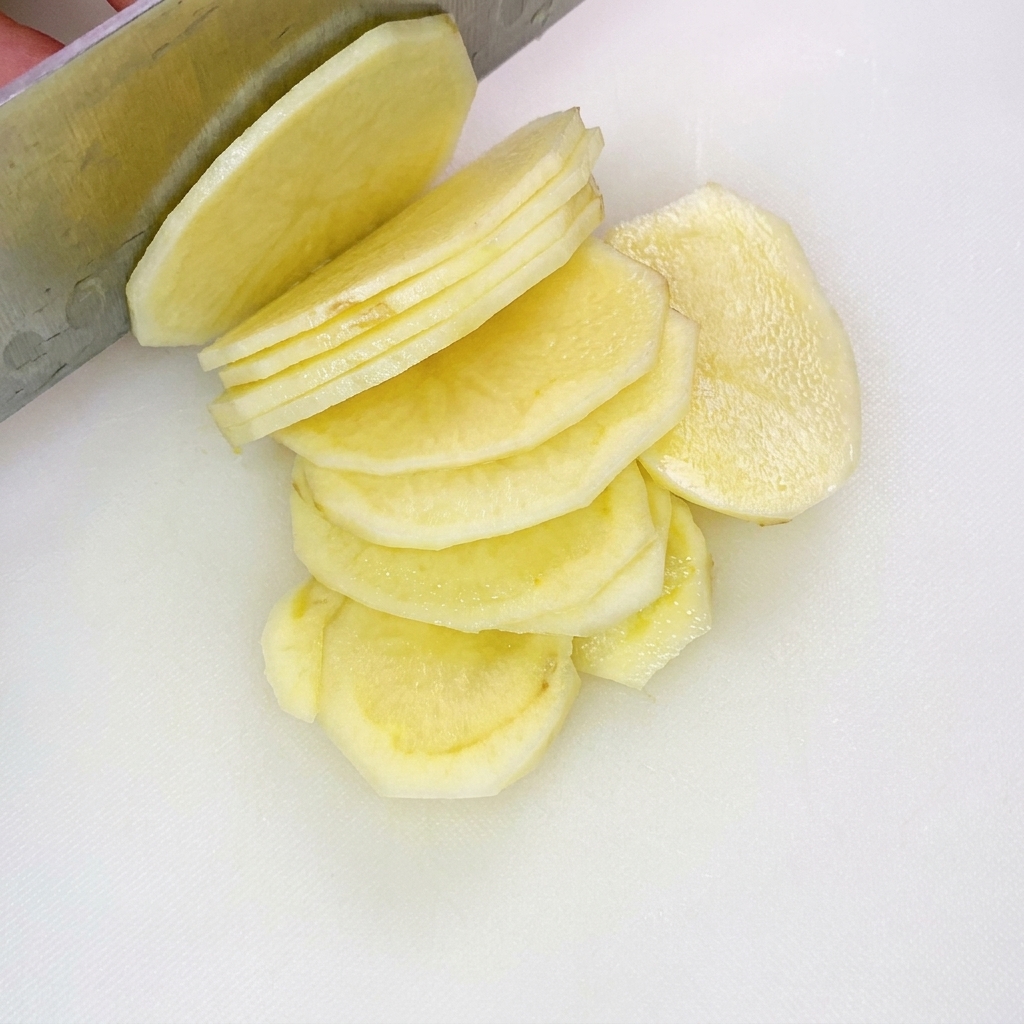 Bâtonnets de pomme de terre fins et uniformes sur une planche à découper blanche.