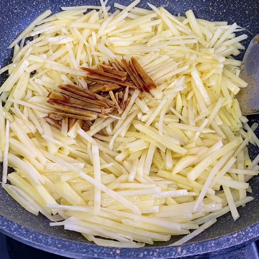 Sauce soja et sauce huître versées sur les pommes de terre sautées dans un wok.