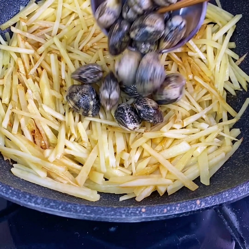 Palourdes fraîches dans leurs coquilles ajoutées au wok avec les pommes de terre assaisonnées.