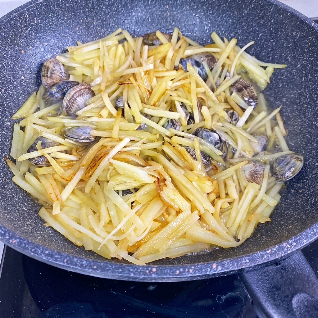 Eau versée dans un wok contenant des bâtonnets de pomme de terre sautés et des palourdes fraîches.