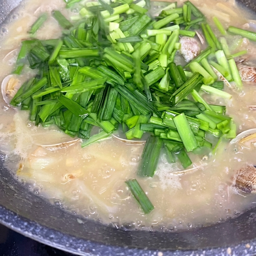 Ciboule chinoise fraîchement hachée saupoudrée sur une marmite de soupe aux pommes de terre et palourdes frémissante.