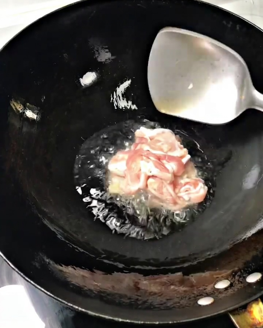 Fines tranches de porc grésillant dans un wok chaud avec de lhuile, remuées avec une spatule en métal.