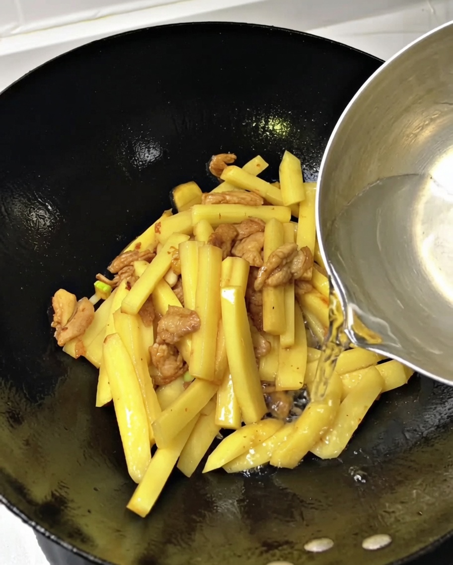 Eau versée dans un wok rempli de lamelles de pommes de terre et de porc.