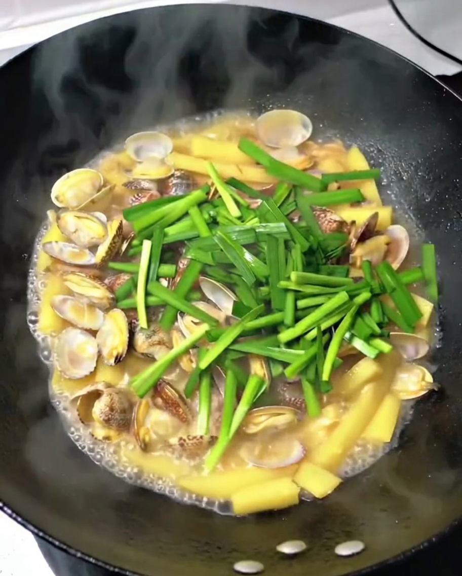 Ciboule aillée fraîche ajoutée dans le wok avec les palourdes, les pommes de terre et le porc.