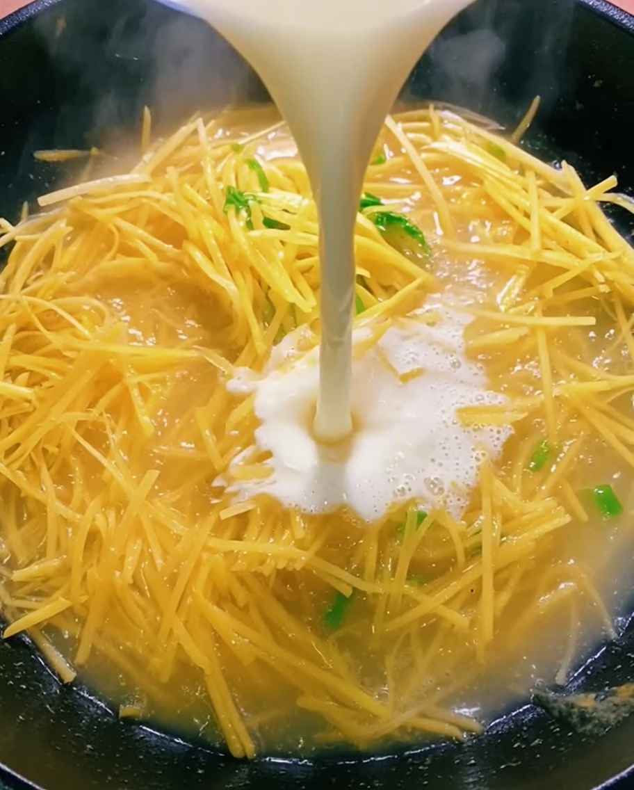 Liquide clair versé dun bol dans un wok contenant des pommes de terre sautées.