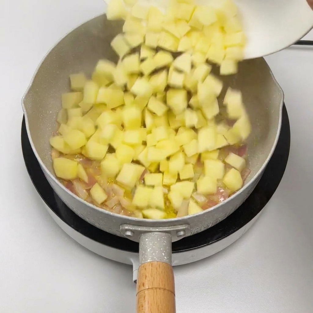 Des dés de pommes de terre glissant dune assiette vers une poêle contenant des oignons rouges sautés.