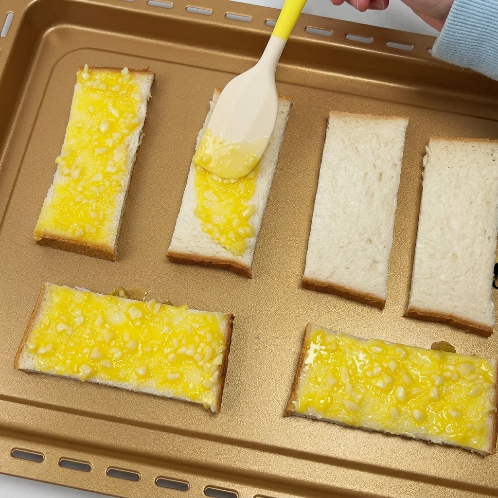 Une spatule étalant du beurre à lail sur des tranches de pain sur une plaque de cuisson.