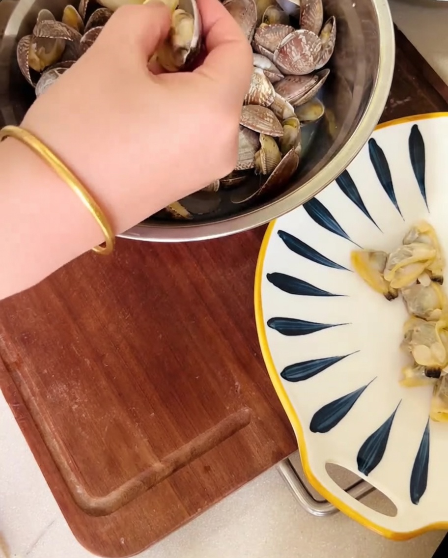 Une main retirant la chair des coquilles de palourdes au-dessus dun bol, avec le bouillon réservé.