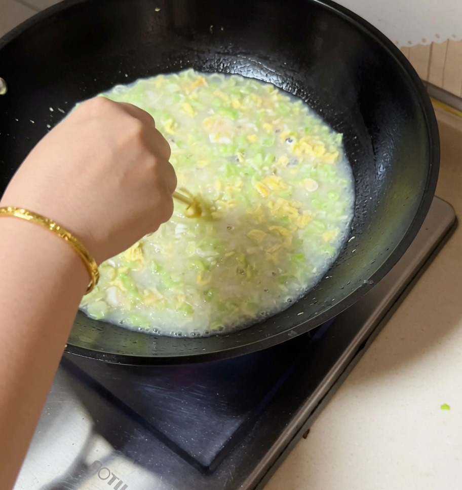 Une main remuant un wok bouillonnant de soupe aux palourdes, haricots rouges et œuf avec des baguettes.