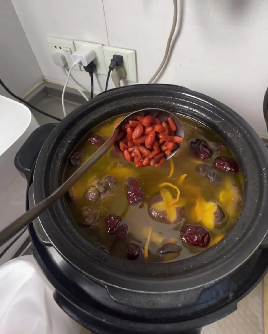 Une louche ajoutant des baies de goji dans la soupe de poulet parfumée.